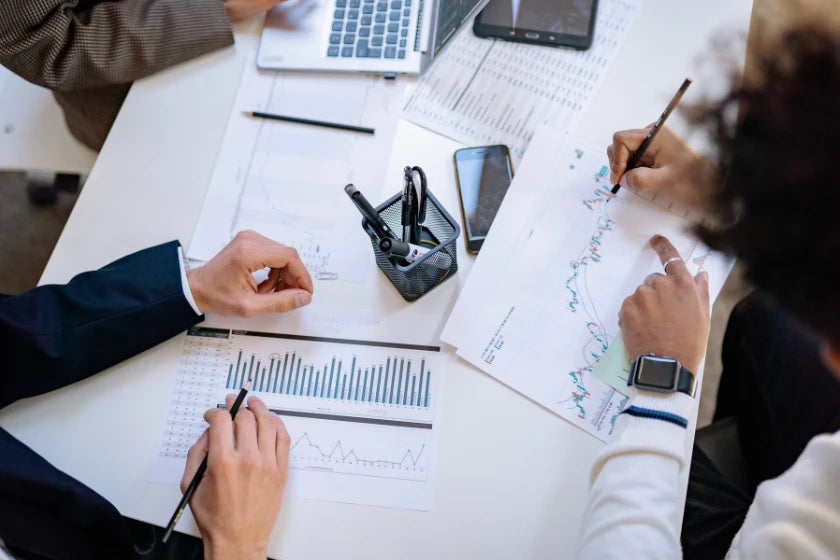 A group of business professionals seated at a table, reviewing documents and taking notes with pens.