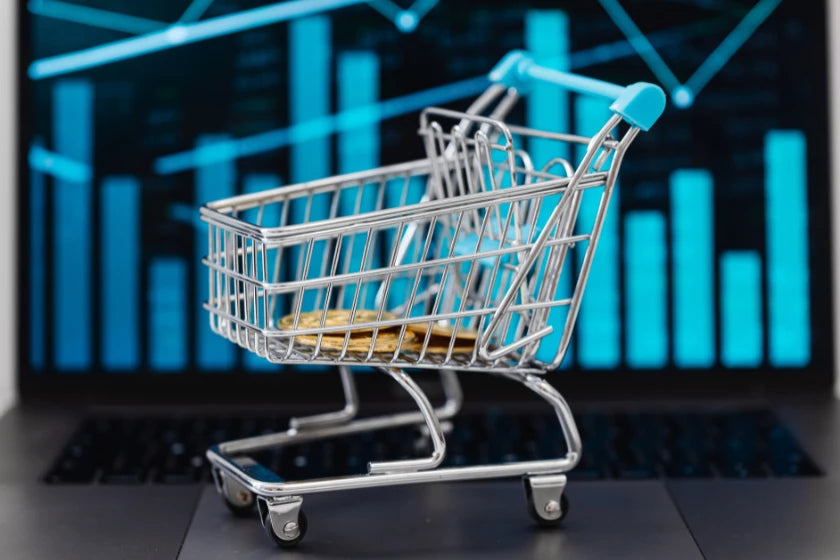 Shopping cart icon filled with gold coins displayed on a laptop screen, symbolizing online shopping and financial transactions.