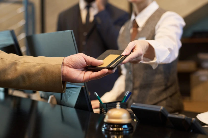 A man hands a credit card to a woman at a hotel reception desk, indicating a transaction or check-in process.