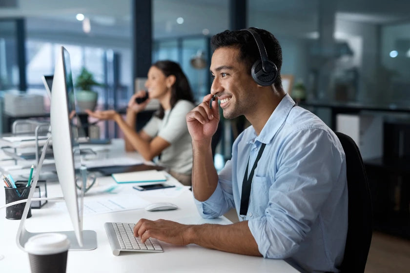 A man wearing headphones sits at a desk in an office, focused on his work.